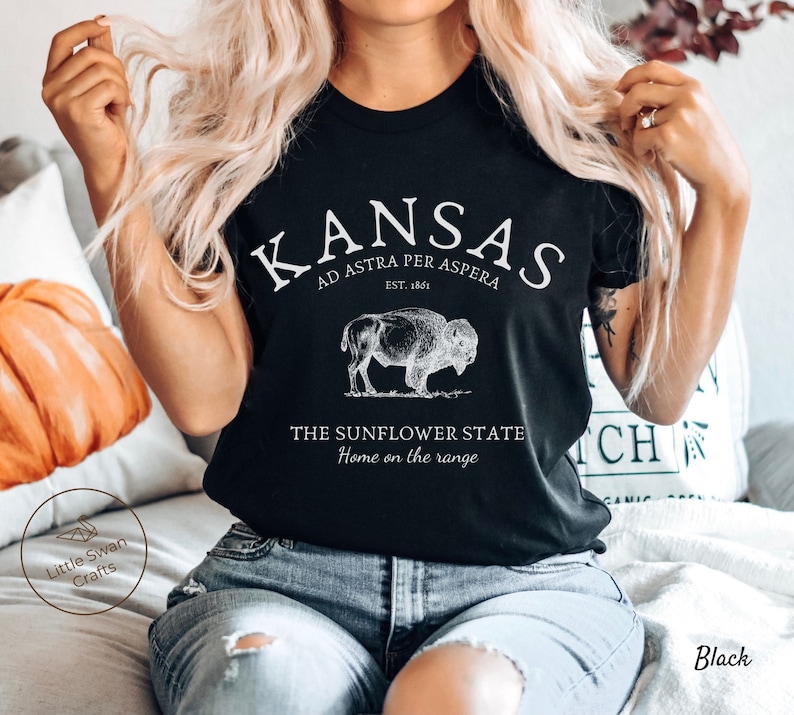 May include: Black t-shirt with white text that reads "Kansas, Ad Astra Per Aspera, Est. 1861, The Sunflower State, Home on the Range". A vintage illustration of a buffalo is above the text.