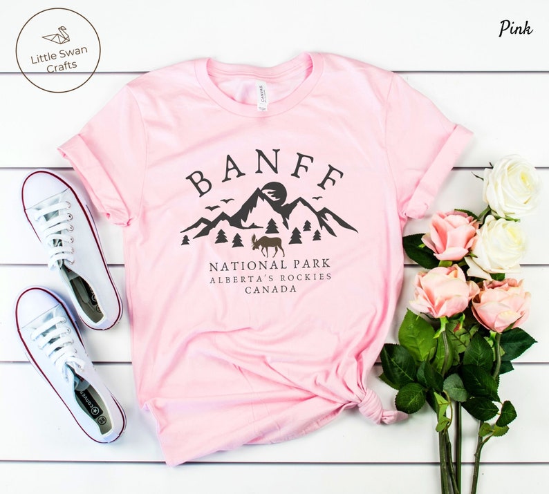 May include: Pink t-shirt with a black graphic design featuring the text "BANFF NATIONAL PARK ALBERTA'S ROCKIES CANADA" and a silhouette of mountains, a sun, and a moose.