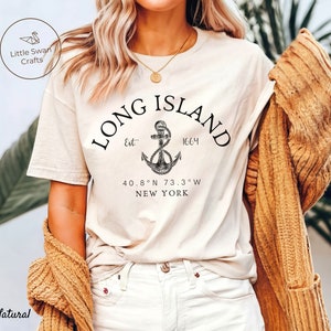 Op de afbeelding: Een wit T-shirt met een zwart grafisch ontwerp van een anker en de tekst "LONG ISLAND Est 1664 40.8&deg;N 73.3&deg;W NEW YORK".