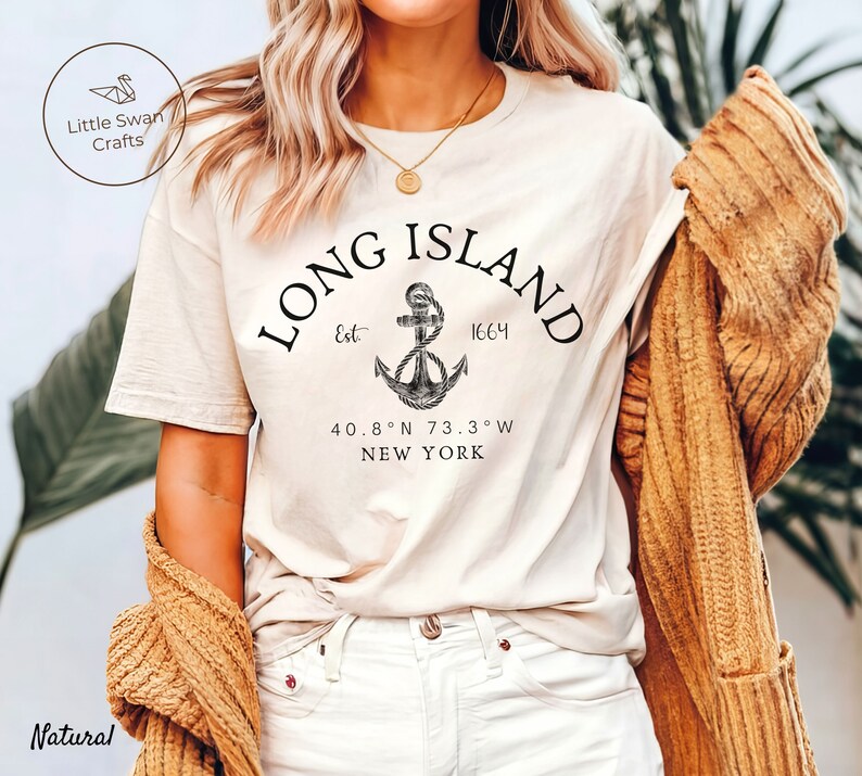 Op de afbeelding: Een wit T-shirt met een zwart grafisch ontwerp van een anker en de tekst "LONG ISLAND Est 1664 40.8&deg;N 73.3&deg;W NEW YORK".