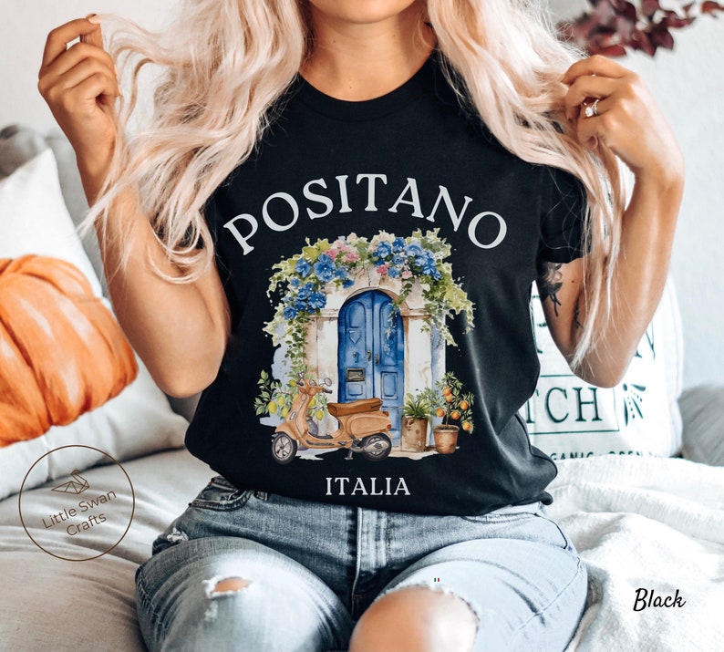 Puede incluir: Camiseta negra con un gr&aacute;fico blanco de una puerta azul con flores y un scooter delante. El texto "Positano Italia" est&aacute; impreso debajo del gr&aacute;fico.