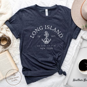 Op de afbeelding: Heather navy blauwe t-shirt met een witte afbeelding van een anker en de tekst "LONG ISLAND Est 1664 40.8&deg;N 73.3&deg;W NEW YORK"