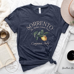 May include: Heather navy t-shirt with the word "Sorrento" and the phrase "The Italian Lemon Town" printed in a light beige color. A lemon branch illustration is below the text. The words "Campania, Italy" are printed below the illustration.
