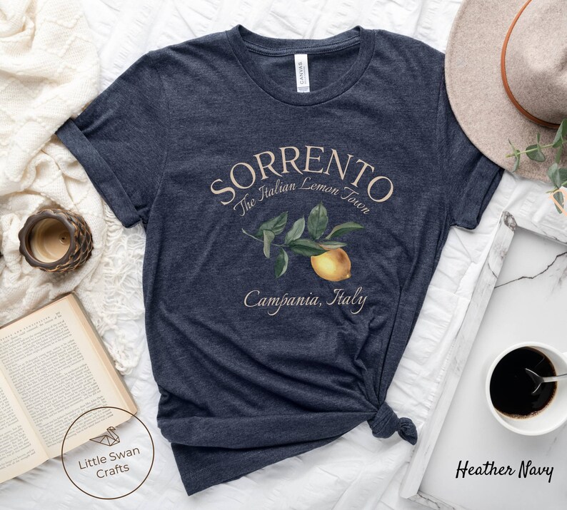 May include: Heather navy t-shirt with the word "Sorrento" and the phrase "The Italian Lemon Town" printed in a light beige color. A lemon branch illustration is below the text. The words "Campania, Italy" are printed below the illustration.