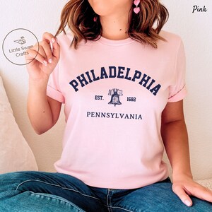 May include: Pink t-shirt with a navy blue graphic of the Liberty Bell and the text "PHILADELPHIA EST. 1682 PENNSYLVANIA".