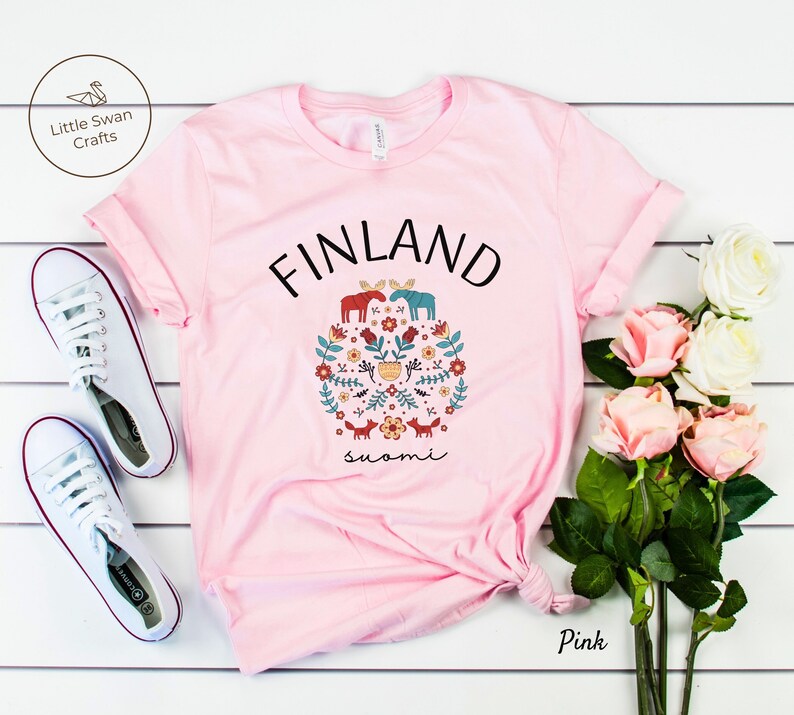 May include: Pink t-shirt with a white graphic design featuring the word "FINLAND" in black text, a circle of stylized flowers, animals, and the word "suomi" in black text.
