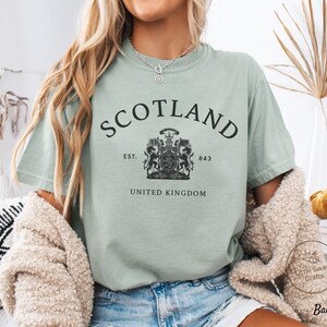 Pode incluir: Camiseta verde claro com a palavra "SCOTLAND" arqueada na parte superior. Abaixo, um bras&atilde;o com "EST. 843" e "UNITED KINGDOM". A camiseta &eacute; feita de um material macio e &eacute; adequada para uso casual.