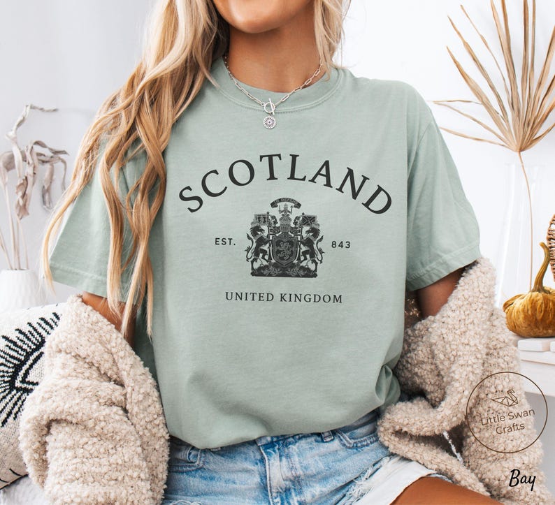 Pode incluir: Camiseta verde claro com a palavra "SCOTLAND" arqueada na parte superior. Abaixo, um bras&atilde;o com "EST. 843" e "UNITED KINGDOM". A camiseta &eacute; feita de um material macio e &eacute; adequada para uso casual.
