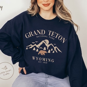 May include: Navy blue sweatshirt with a graphic design of a mountain range and a bear. The text "Grand Teton National Park" and "Wyoming Est. 1929" is printed on the sweatshirt.