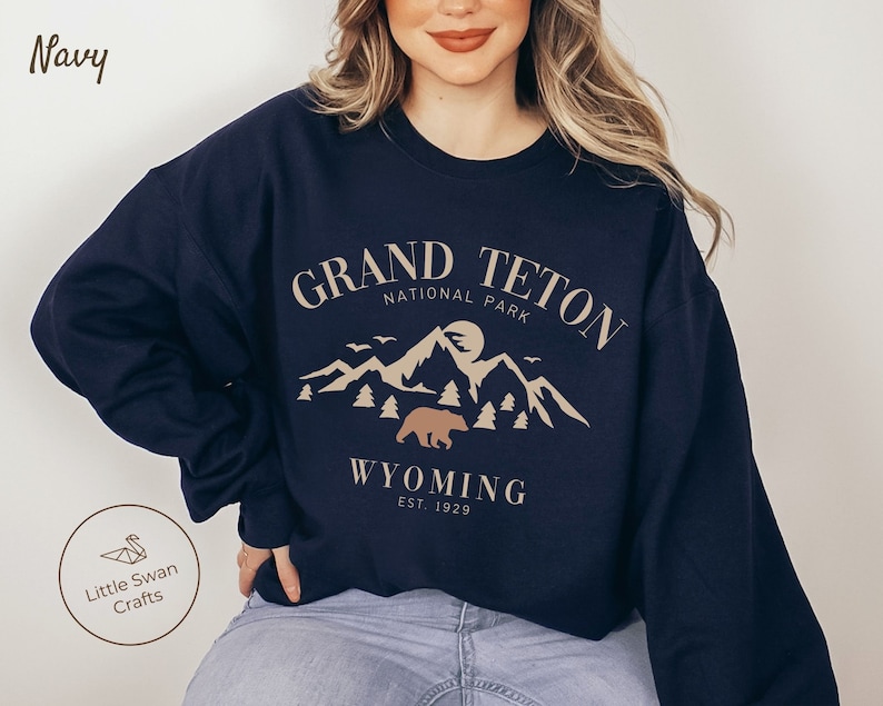 May include: Navy blue sweatshirt with a graphic design of a mountain range and a bear. The text "Grand Teton National Park" and "Wyoming Est. 1929" is printed on the sweatshirt.