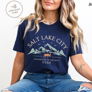 May include: A navy blue t-shirt with a graphic design of mountains, a moose, and the text "Salt Lake City, Crossroads of the West, Utah".