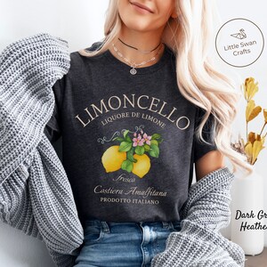 May include: Dark grey heather t-shirt with a vintage-style illustration of lemons and blossoms. The text "LIMONCELLO LIQUORE DE LIMONE" is printed in a white script font. The text "Fresco Costiera Amalfitana PRODOTTO ITALIANO" is printed in a smaller white font.