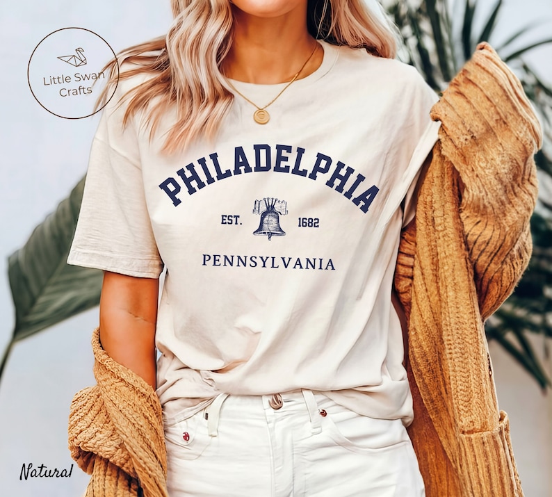 May include: A white t-shirt with a navy blue graphic of the Liberty Bell and the text "PHILADELPHIA EST. 1682 PENNSYLVANIA".