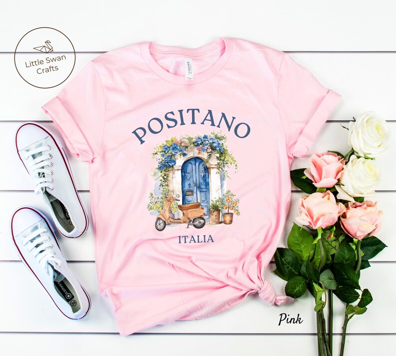 Puede incluir: Camiseta rosa con un gr&aacute;fico de una puerta azul y un scooter. El texto "Positano Italia" est&aacute; impreso en la camiseta.