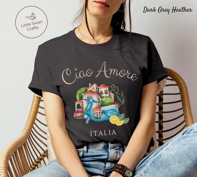 May include: Dark grey heather t-shirt with a watercolor illustration of a scooter, a small house, and lemons. The text "Ciao Amore" and "ITALIA" are printed on the shirt.