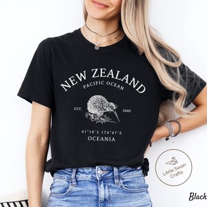 Peut inclure: T-shirt noir avec un motif blanc repr&eacute;sentant un kiwi, le texte "NEW ZEALAND", "PACIFIC OCEAN", "EST. 1840", "41&deg;18&prime;S 174&deg;47&prime;E", et "OCEANIA".