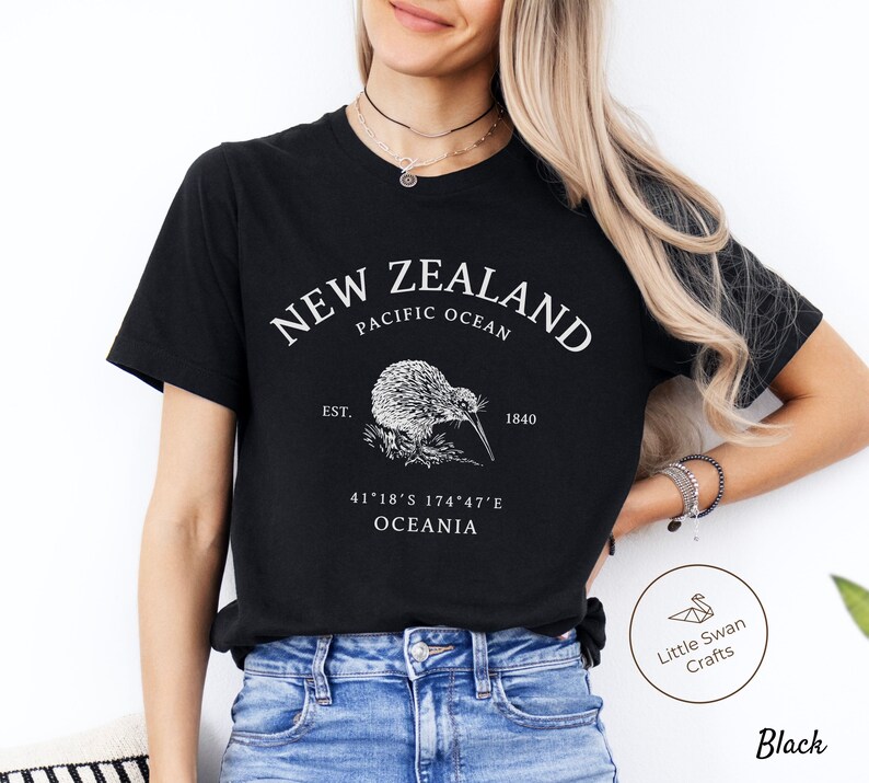 Peut inclure: T-shirt noir avec un motif blanc repr&eacute;sentant un kiwi, le texte "NEW ZEALAND", "PACIFIC OCEAN", "EST. 1840", "41&deg;18&prime;S 174&deg;47&prime;E", et "OCEANIA".