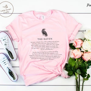 Puede incluir: Camiseta rosa con una ilustraci&oacute;n de cuervo negro y el texto "THE RAVEN" y la primera estrofa del poema "El Cuervo" de Edgar Allan Poe.