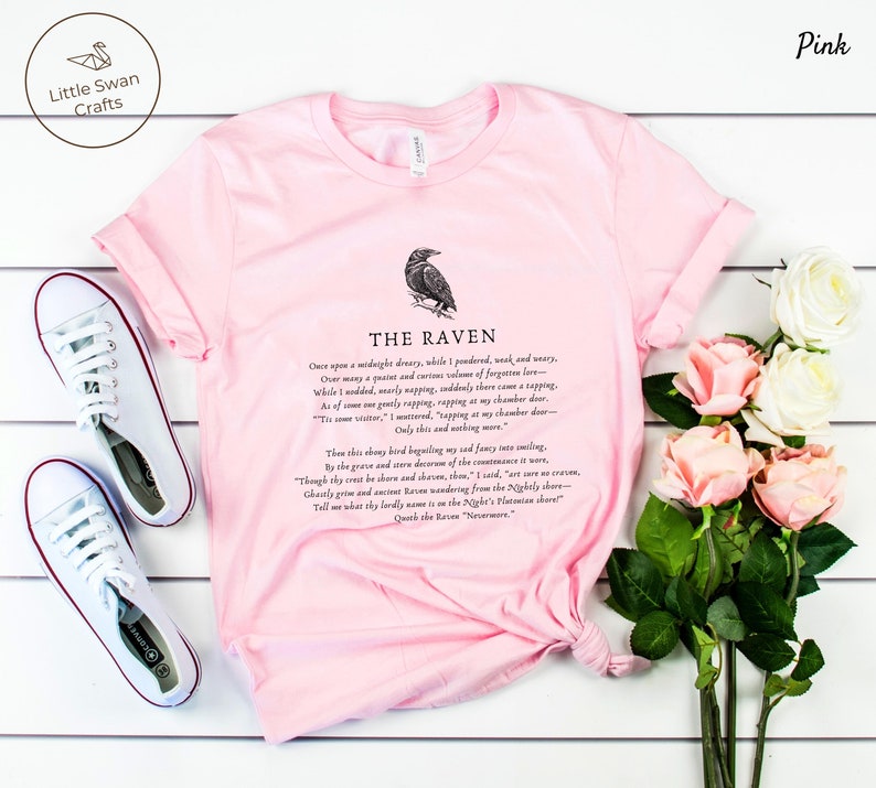 Puede incluir: Camiseta rosa con una ilustraci&oacute;n de cuervo negro y el texto "THE RAVEN" y la primera estrofa del poema "El Cuervo" de Edgar Allan Poe.