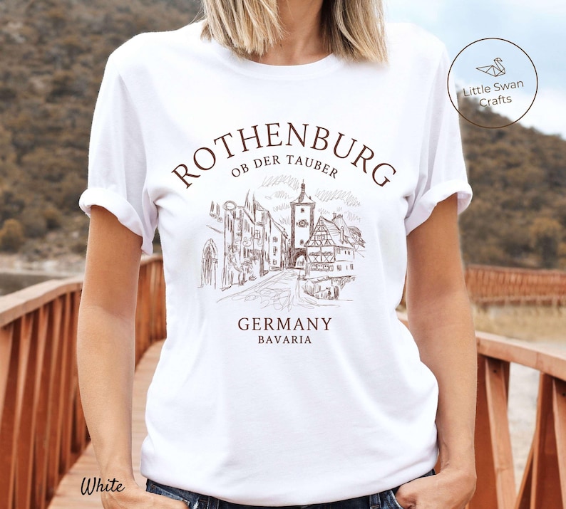 Pode incluir: Camiseta branca com um gr&aacute;fico marrom de uma cidade alem&atilde; com o texto "Rothenburg ob der Tauber, Alemanha, Baviera".