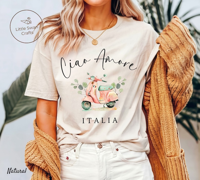 May include: A white t-shirt with a watercolor illustration of a pink scooter with green leaves and the text "Ciao Amore ITALIA".