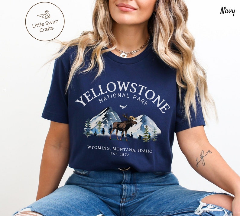 May include: Navy blue t-shirt featuring a Yellowstone National Park design. The graphic includes mountains, a moose, and the text "YELLOWSTONE NATIONAL PARK" with "WYOMING, MONTANA, IDAHO EST. 1872" below. The shirt is a short-sleeved crew neck.
