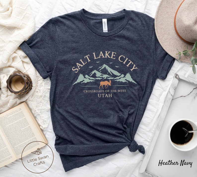 May include: Heather navy blue t-shirt with a graphic design of a mountain range with a moose and the text "Salt Lake City, Crossroads of the West, Utah".