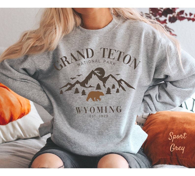 May include: Gray sweatshirt with a brown graphic design of mountains, a bear, and the text "Grand Teton National Park Wyoming Est. 1929."