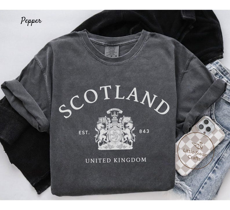 Pode incluir: Um moletom cinza escuro com gola redonda e a palavra "SCOTLAND" em branco. Abaixo, um bras&atilde;o e o texto "EST. 843 UNITED KINGDOM". O moletom est&aacute; dobrado sobre uma superf&iacute;cie clara.