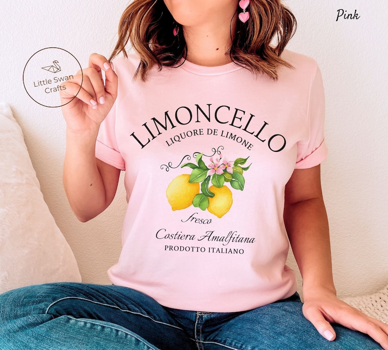 May include: Pink t-shirt with a graphic design of lemons and a lemon tree branch. The text on the shirt reads "Limoncello Liquore de Limone Fresco Costiera Amalfitana Prodotto Italiano".