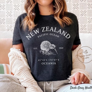 Peut inclure: T-shirt gris fonc&eacute; chin&eacute; avec un graphique blanc d'un kiwi et le texte "NEW ZEALAND", "PACIFIC OCEAN", "EST. 1840", "41&deg;18'S 174&deg;47'E", et "OCEANIA".