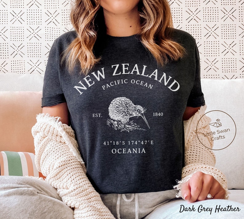 Peut inclure: T-shirt gris fonc&eacute; chin&eacute; avec un graphique blanc d'un kiwi et le texte "NEW ZEALAND", "PACIFIC OCEAN", "EST. 1840", "41&deg;18'S 174&deg;47'E", et "OCEANIA".