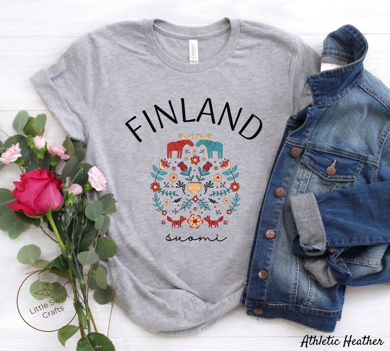 May include: A heather grey t-shirt with a black and white graphic design of a moose, flowers, and foxes. The text "FINLAND" is above the graphic and the text "suomi" is below the graphic.