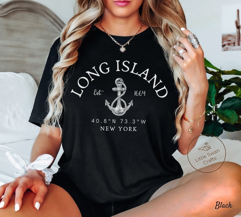 Op de afbeelding: Zwart T-shirt met een witte afbeelding van een anker en de tekst "LONG ISLAND Est 1664 40.8&deg;N 73.3&deg;W NEW YORK".