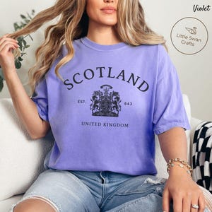 Pode incluir: Uma t-shirt violeta com a palavra "SCOTLAND" impressa em preto no peito. Abaixo, um bras&atilde;o e as palavras "EST. 843" e "UNITED KINGDOM". A t-shirt tem um corte folgado.