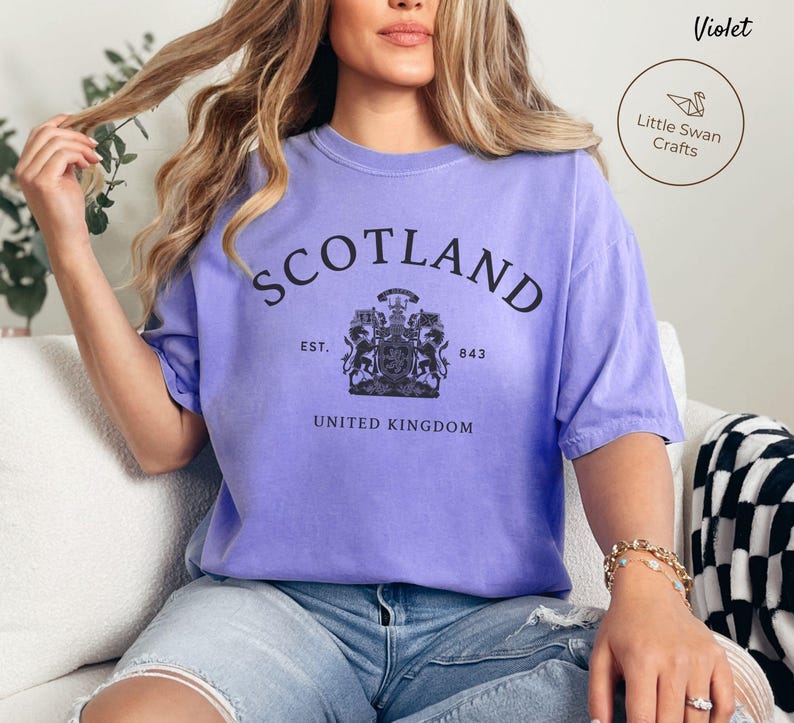Pode incluir: Uma t-shirt violeta com a palavra "SCOTLAND" impressa em preto no peito. Abaixo, um bras&atilde;o e as palavras "EST. 843" e "UNITED KINGDOM". A t-shirt tem um corte folgado.