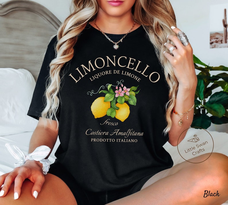 May include: Black t-shirt with a graphic of lemons and flowers. The text "Limoncello Liquore de Limone Fresco Costiera Amalfitana Prodotto Italiano" is printed on the shirt.