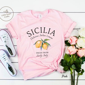 Peut inclure: T-shirt rose avec un motif graphique de citrons et le texte "SICILIA Delicious Italian Lemons Fresh From Sicily, Italy".