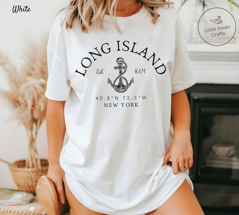 Op de afbeelding: Wit T-shirt met een zwart grafisch ontwerp met de tekst "LONG ISLAND" in een boog boven een anker met de tekst "Est 1664" en "40.8&deg;N 73.3&deg;W NEW YORK" onder het anker.
