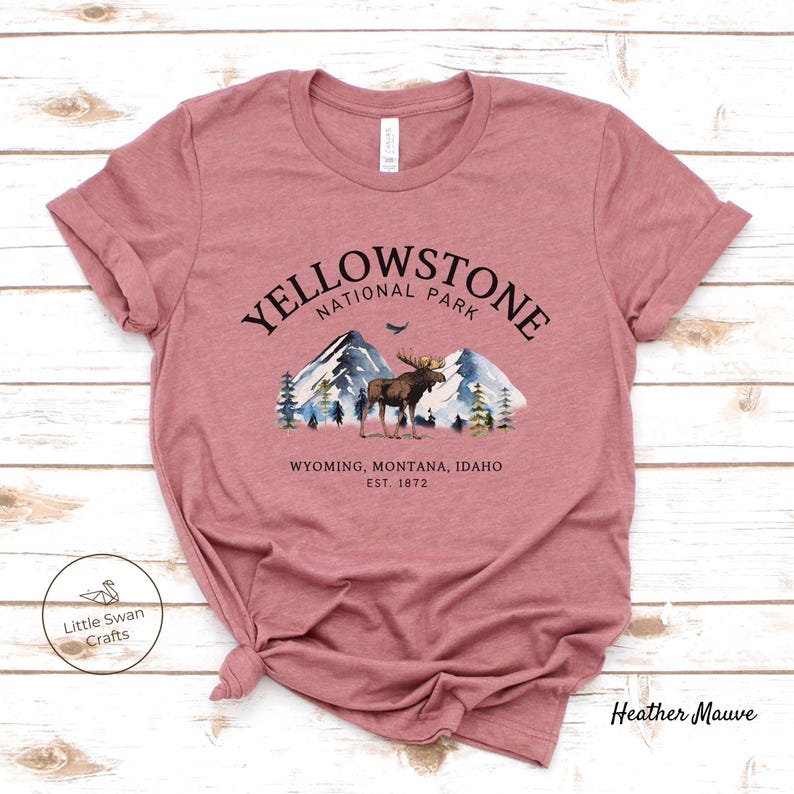 May include: Heather mauve t-shirt featuring a graphic of Yellowstone National Park. The design includes mountains, trees, and a moose, with the text "YELLOWSTONE NATIONAL PARK" and "WYOMING, MONTANA, IDAHO EST. 1872".