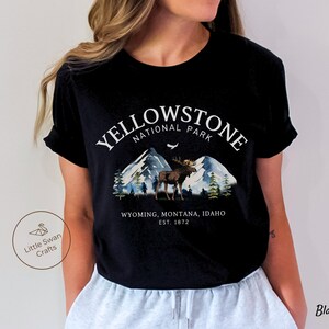 May include: Black t-shirt featuring a Yellowstone National Park design. The graphic includes mountains, a moose, and the text "YELLOWSTONE NATIONAL PARK" above "WYOMING, MONTANA, IDAHO EST. 1872". The shirt is a classic crew neck.
