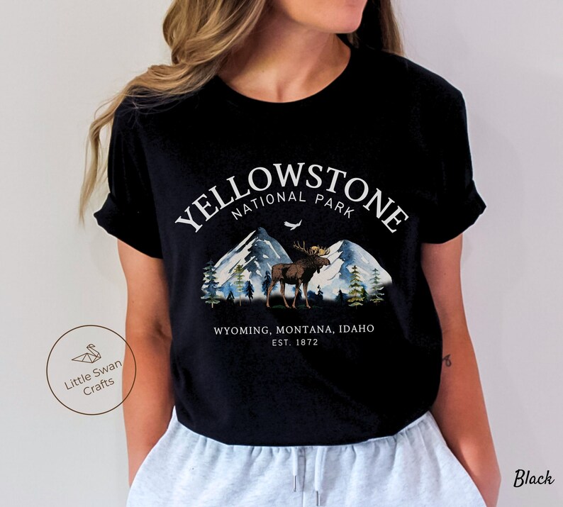 May include: Black t-shirt featuring a Yellowstone National Park design. The graphic includes mountains, a moose, and the text "YELLOWSTONE NATIONAL PARK" above "WYOMING, MONTANA, IDAHO EST. 1872". The shirt is a classic crew neck.