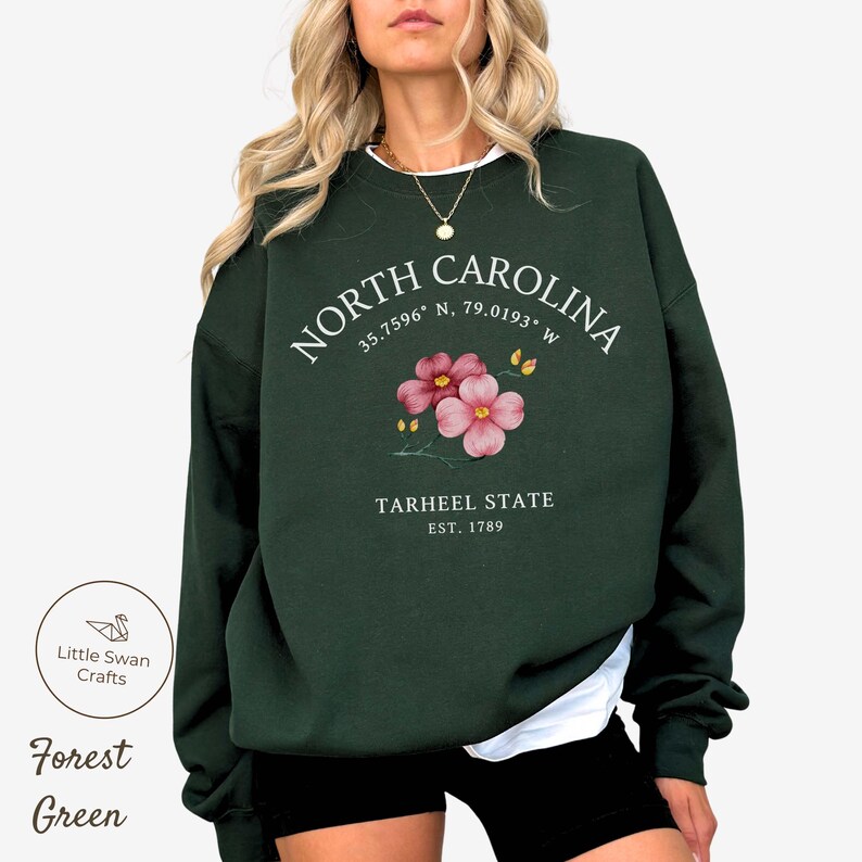 May include: Forest green sweatshirt with the text "NORTH CAROLINA" and coordinates, a floral design, and "TARHEEL STATE EST. 1789". The sweatshirt is a dark green color.