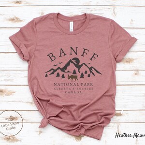 May include: Heather mauve t-shirt with a black graphic design of mountains, a moose, and the text "Banff National Park, Alberta's Rockies, Canada".