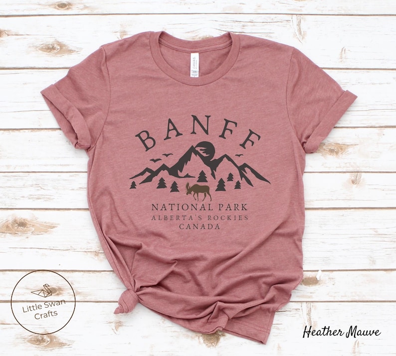 May include: Heather mauve t-shirt with a black graphic design of mountains, a moose, and the text "Banff National Park, Alberta's Rockies, Canada".