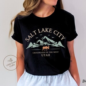 May include: Black t-shirt with a graphic design featuring the text "Salt Lake City, Crossroads of the West, Utah" with a mountain range and a moose silhouette.