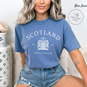 Pode incluir: Camiseta azul jeans com a palavra "SCOTLAND" em letras brancas. Abaixo, um bras&atilde;o com as palavras "EST. 843" e "UNITED KINGDOM". A camiseta tem mangas curtas e gola redonda.