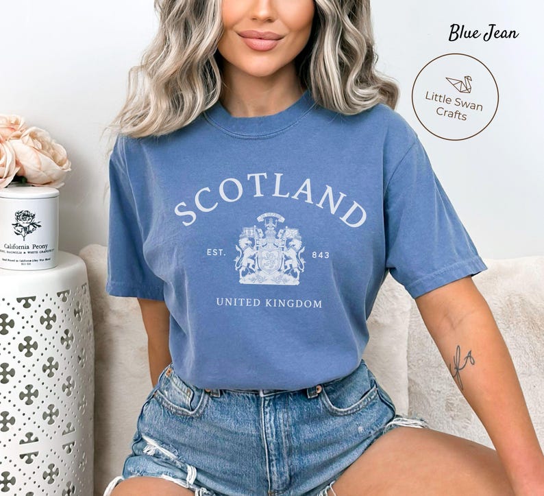 Pode incluir: Camiseta azul jeans com a palavra "SCOTLAND" em letras brancas. Abaixo, um bras&atilde;o com as palavras "EST. 843" e "UNITED KINGDOM". A camiseta tem mangas curtas e gola redonda.