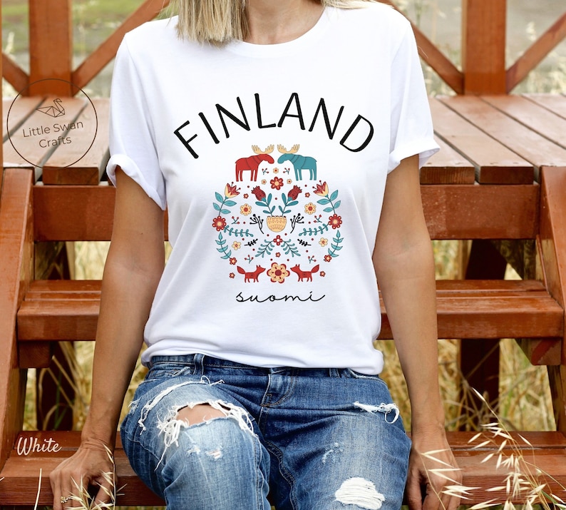 May include: White t-shirt with a graphic design featuring the word "FINLAND" in black text, a floral pattern with red, blue, and yellow accents, and the word "suomi" in black text.