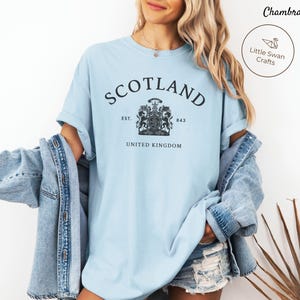 Pode incluir: Camiseta azul clara com a palavra "SCOTLAND" em arco e um desenho de bras&atilde;o abaixo. O texto "EST. 843 UNITED KINGDOM" est&aacute; abaixo do bras&atilde;o. Parte de uma cole&ccedil;&atilde;o de roupas.
